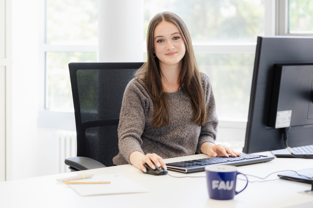 Auszubildende im Bereich Büromanagement arbeitet an einem Computer in einem modernen, hellen Büro.