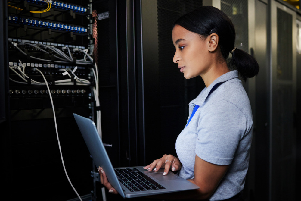 Eine Auszubildende für Fachinformatik - Systemintegration steht mit einem Laptop in einem Serverraum.