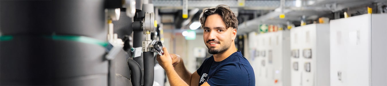 Auszubildender im Bereich Anlagenmechanik steht an einer Kühlungsanlage und repariert diese mit einem Werkzeug