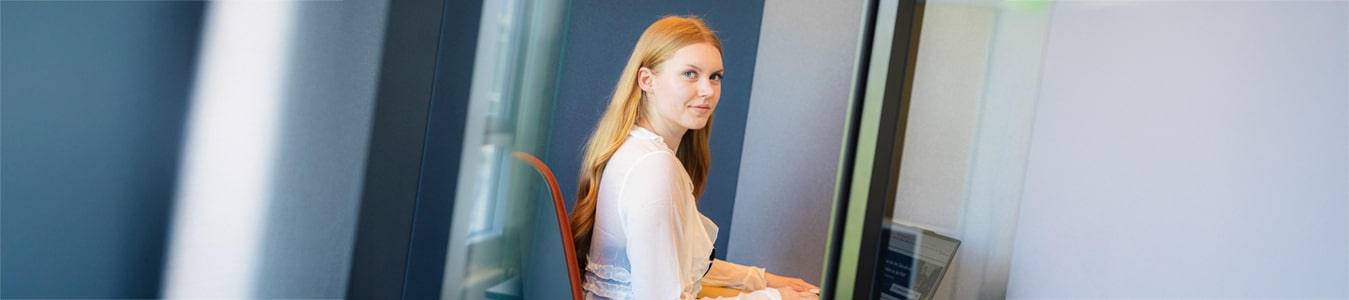 Auszubildende sitzt in einem modernen Büro an einem Schreibtisch, auf dem ein Laptop vor ihr steht