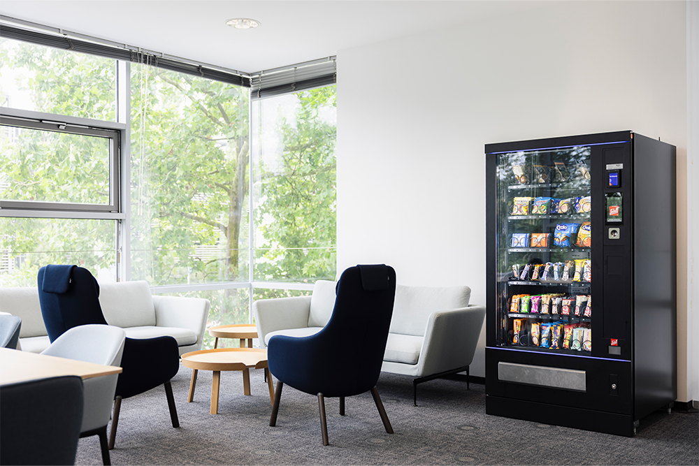 Blick in ein Work Café der Friedrich-Alexander-Universität Erlangen-Nürnberg. Darin befinden sich Stühle und eine Couch sowie ein Snackautomat.