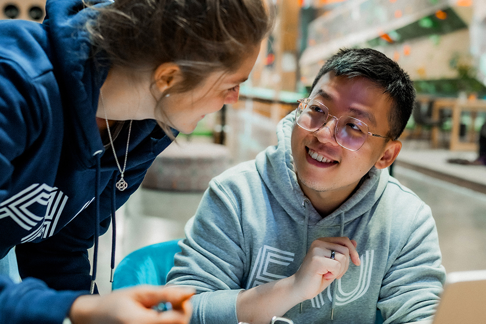 Zwei Studierende der FAu-Erlangen-Nürnberg unterhalten sich miteinander. Beide tragen einen Pullover mit dem FAU-Logo.