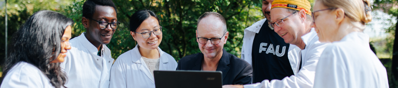Eine Gruppe Forschender in weißen Kittel steht über einem Laptop zusammen.