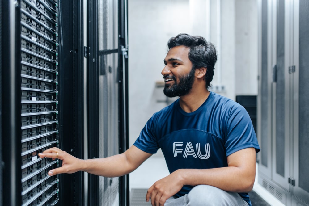 Eine männlich gelesene Person kniet an einem Serverschrank in einem Serverraum.