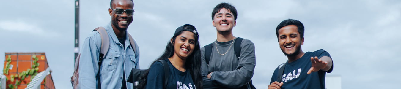 Eine Gruppe von vier jungen, diversen Personen lächelt in die Kamera. Sie sind outdoor und tragen Rucksäcke sowie legere Kleidung.