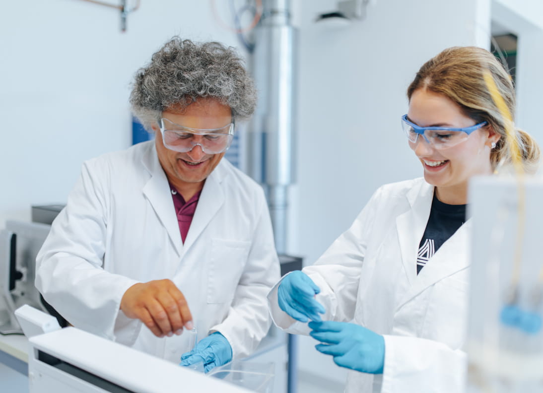 Zwei Personen in weißen Kitteln und mit Schutzbrillen experimentieren in einem Forschungslabor.